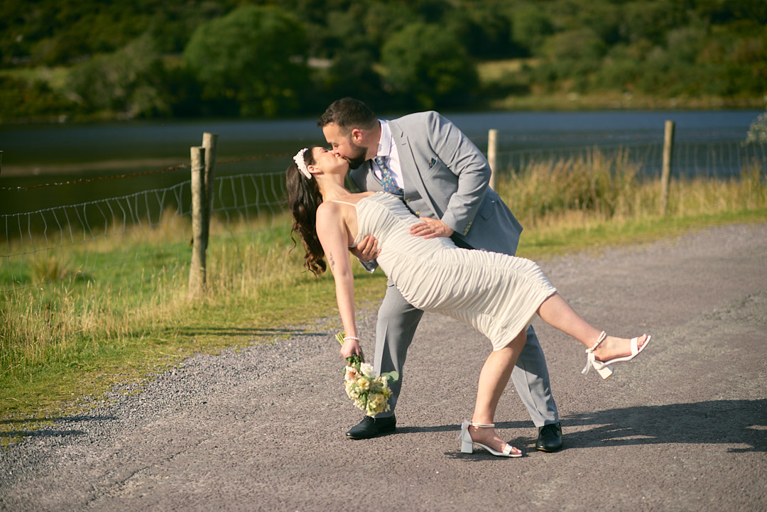 Black and white shot of a bride and groom walking toward the camera on a big gravel path. They are holding hands, deep in conversation. Background is covered in thick trees